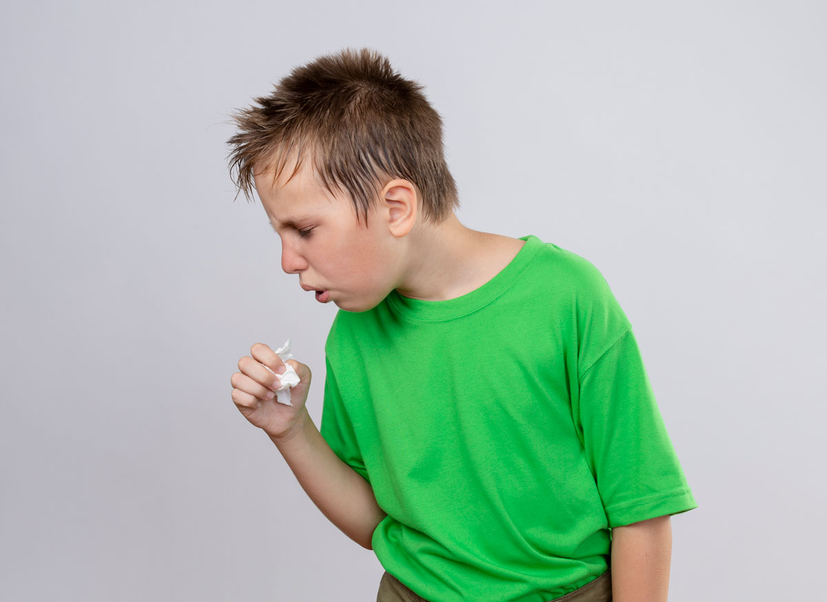 ill little boy green t shirt feeling unwell coughing standing white wall